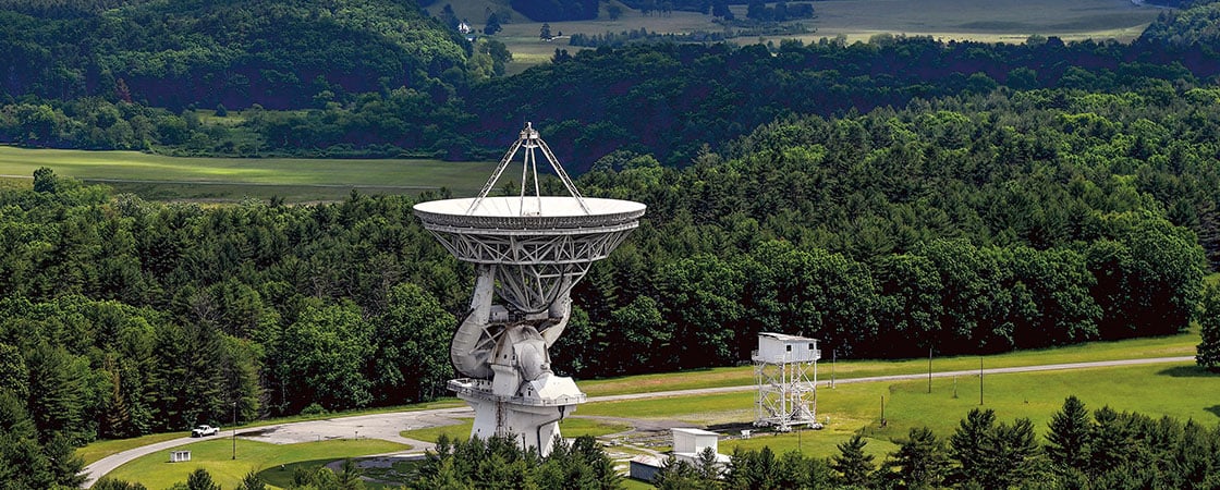 a large telescope standing front of green trees and a mountain