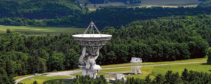 a large telescope standing front of green trees and a mountain