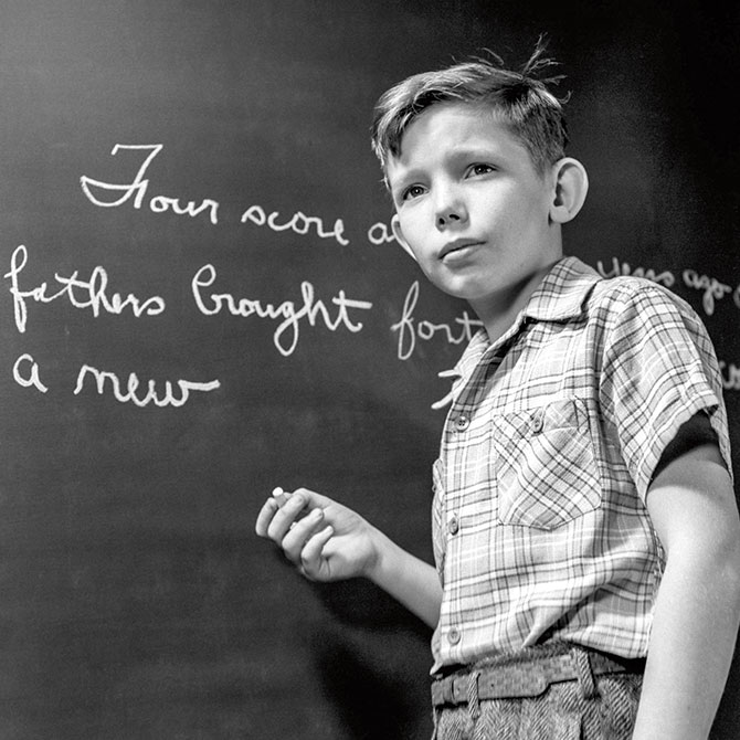 enlargeable black and white photo of a student writing in cursive on a chalkboard