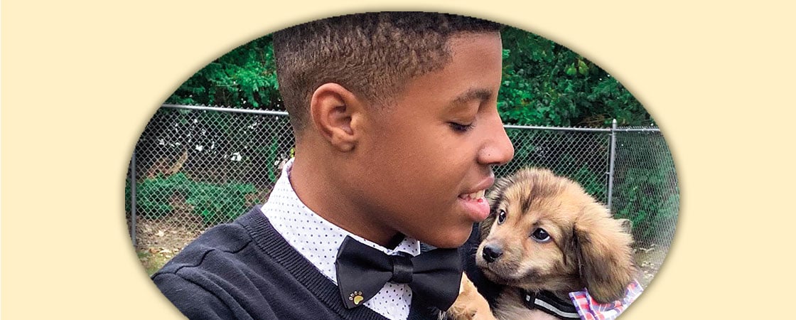 A boy holding a small dog. Both the boy and dog are wearing bow ties. 