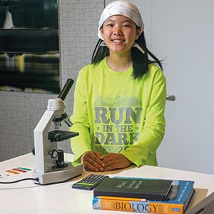 Photo of a student with a microscope and books